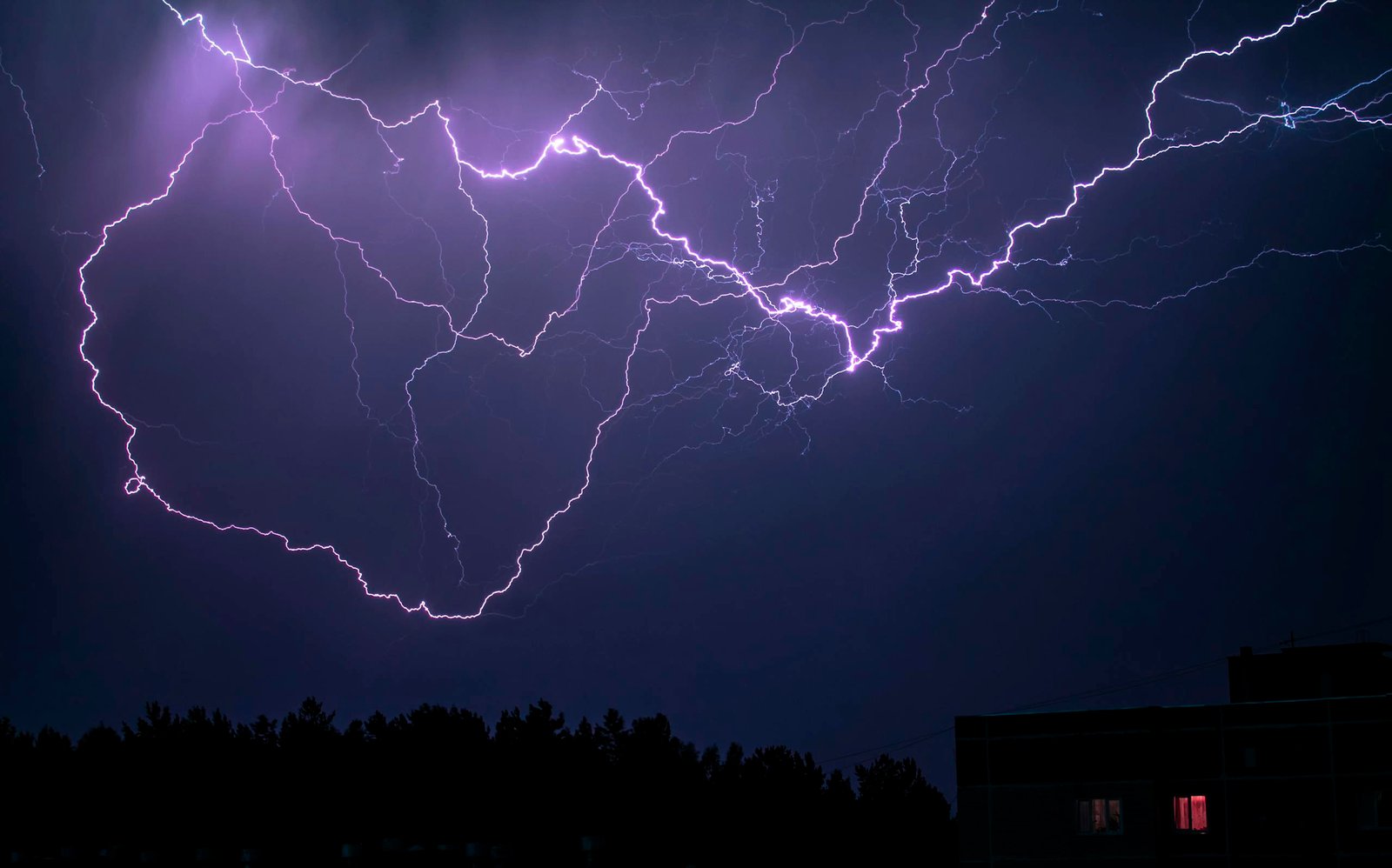 A breathtaking lightning storm at night over a forest with vivid flashes in the sky.
